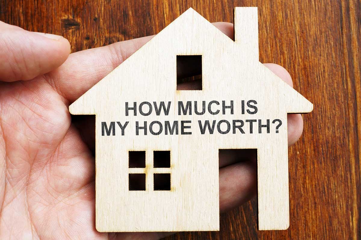 wooden cut out of a house with the question "how much is my home worth?" printed on it used to describe the difference between a home inspection vs appraisal